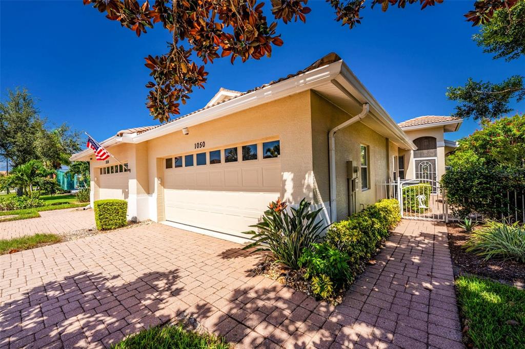 A beige house with a two-car garage, a brick driveway, and a gated side entrance — 1050 YOSEMITE DRIVE, ENGLEWOOD, FL