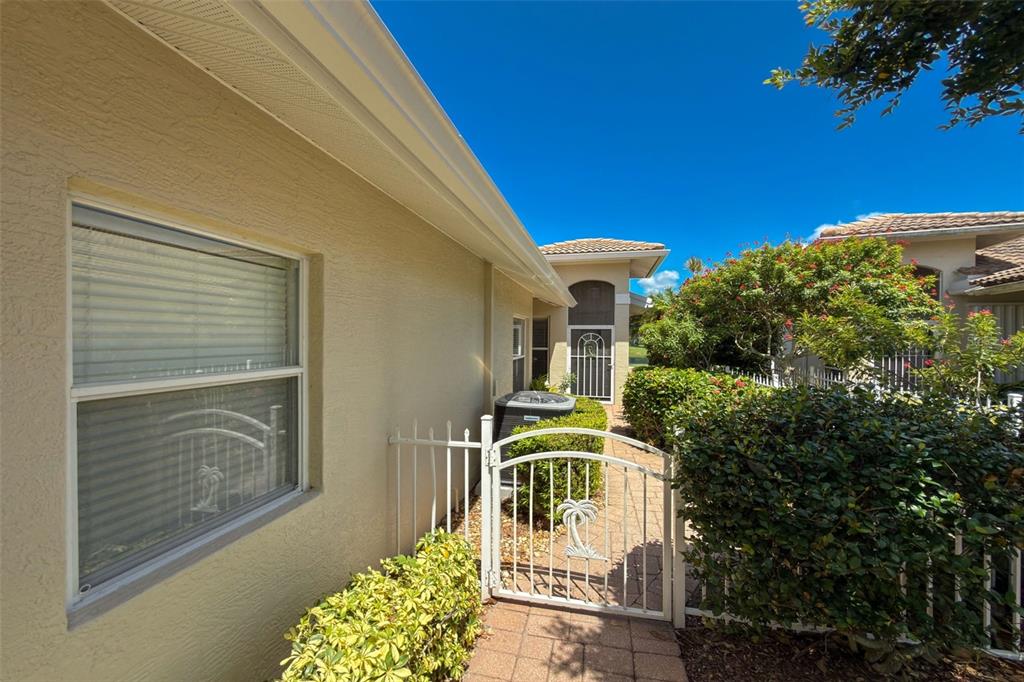 A paved walkway leads through a white metal gate toward the side entrance of a house — 1050 YOSEMITE DRIVE, ENGLEWOOD, FL
