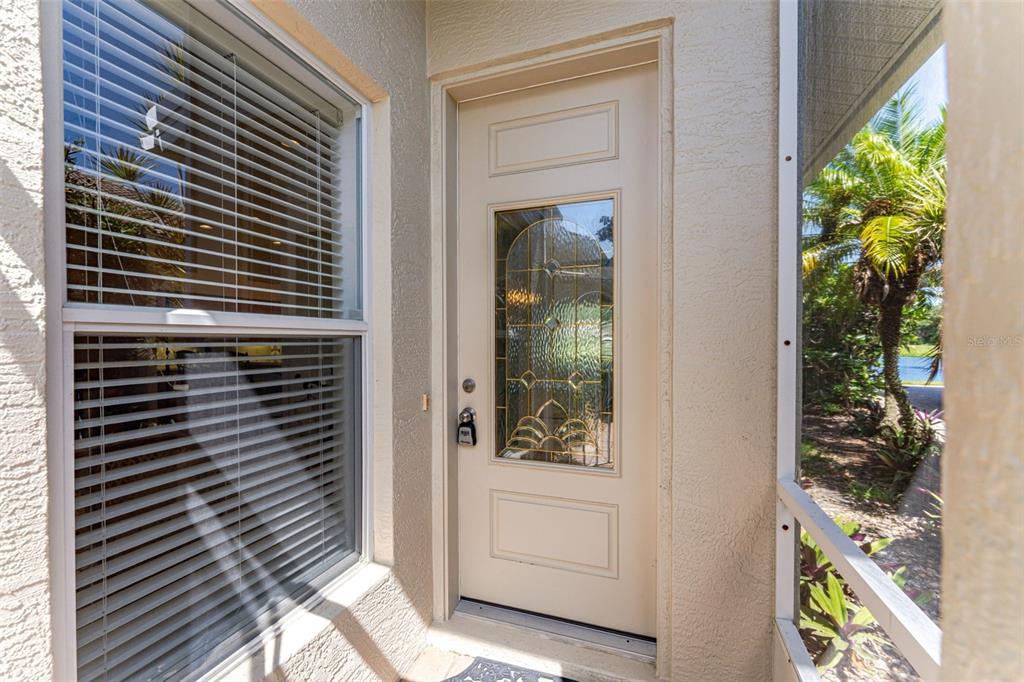 A beige front door with a decorative glass insert sits beside a window with blinds — 1050 YOSEMITE DRIVE, ENGLEWOOD, FL