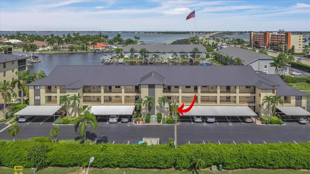 An aerial view of a multi-story apartment building with covered parking and a waterfront location — 4719 SE 17TH PLACE UNIT 105, CAPE CORAL, FL