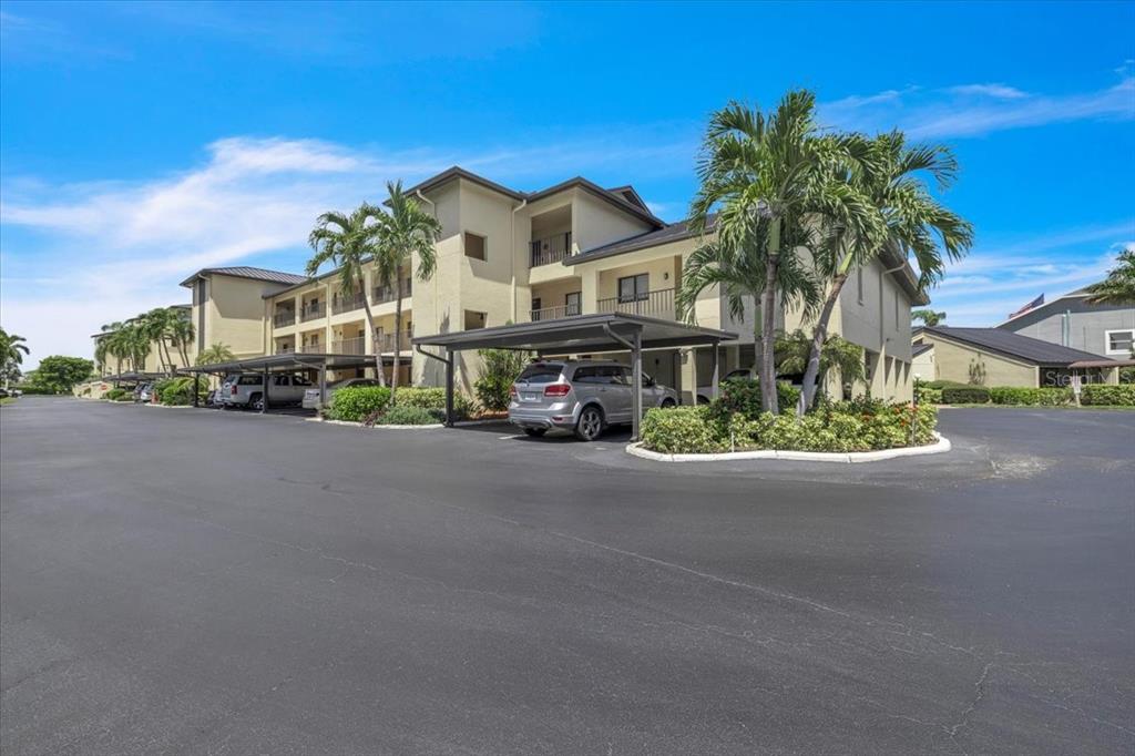 A multi-story apartment building with covered parking and palm trees in a paved lot — 4719 SE 17TH PLACE UNIT 105, CAPE CORAL, FL