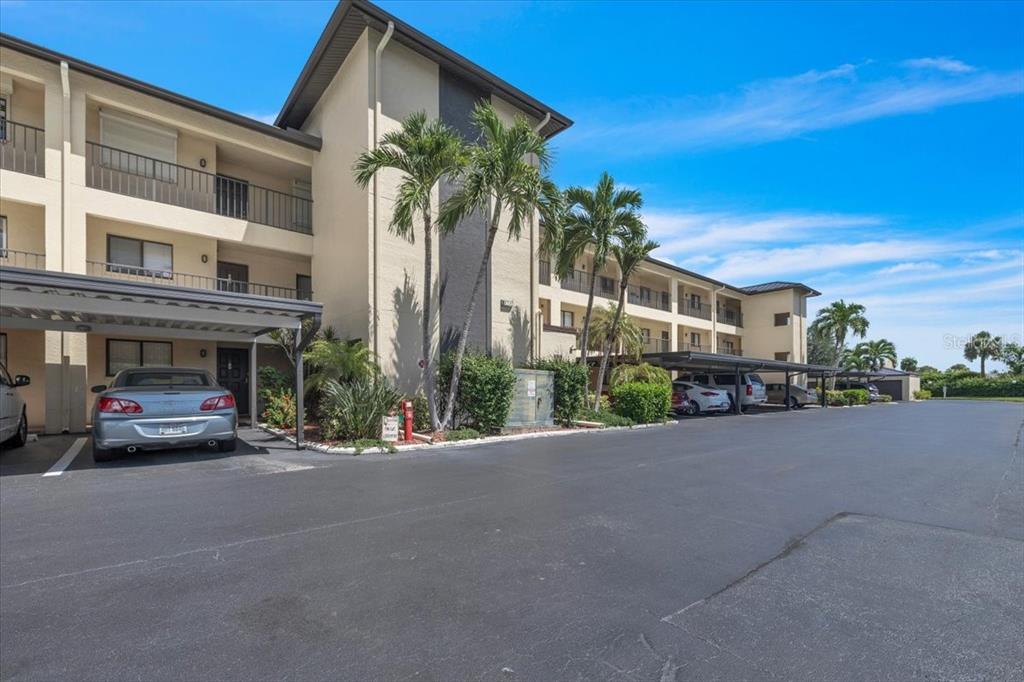 A multi-story apartment building with covered parking spaces and palm trees in the foreground — 4719 SE 17TH PLACE UNIT 105, CAPE CORAL, FL