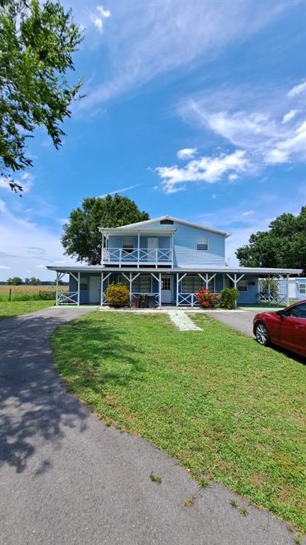 A two-story light blue house with a wrap-around porch and a balcony sits on grass — 6275 US-441 HIGHWAY SE, OKEECHOBEE, FL