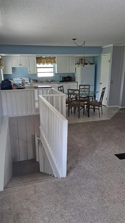 A kitchen and dining area overlook a carpeted staircase with white wooden railings — 6275 US-441 HIGHWAY SE, OKEECHOBEE, FL