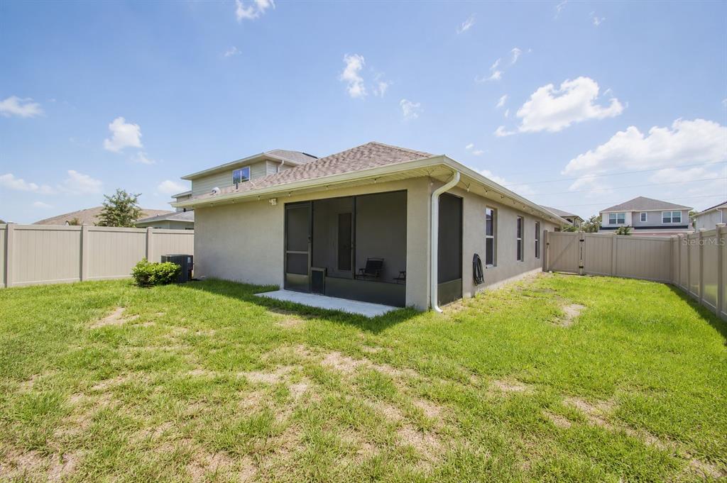 The backyard features a tan house with a screened-in porch and a vinyl privacy fence — 3675 SAGEFIELD DRIVE, HARMONY, FL