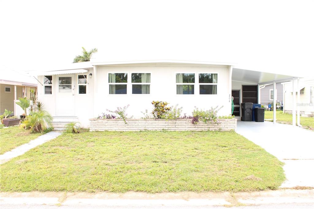 A white single-story manufactured home features a front lawn, a brick planter, and a carport — 204 50TH AVENUE DRIVE W, BRADENTON, FL