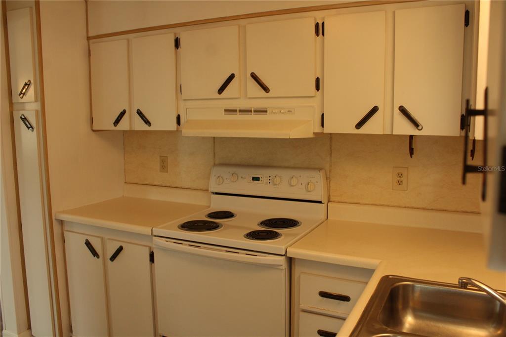 A kitchen features white cabinets, a white electric stove, and a stainless steel sink — 204 50TH AVENUE DRIVE W, BRADENTON, FL
