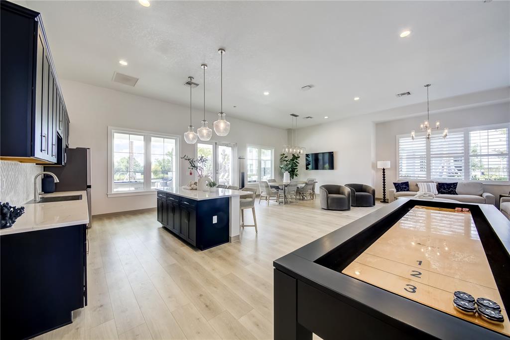 A spacious open-concept room features a kitchen island, dining area, lounge seating, and shuffleboard table — 9131 WALCOTT LANE, LAKEWOOD RANCH, FL