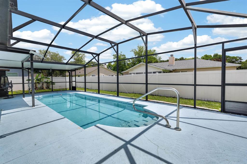 A screened-in swimming pool with a metal handrail sits on a concrete patio — 20 LAKE MEADOW WAY, ORMOND BEACH, FL