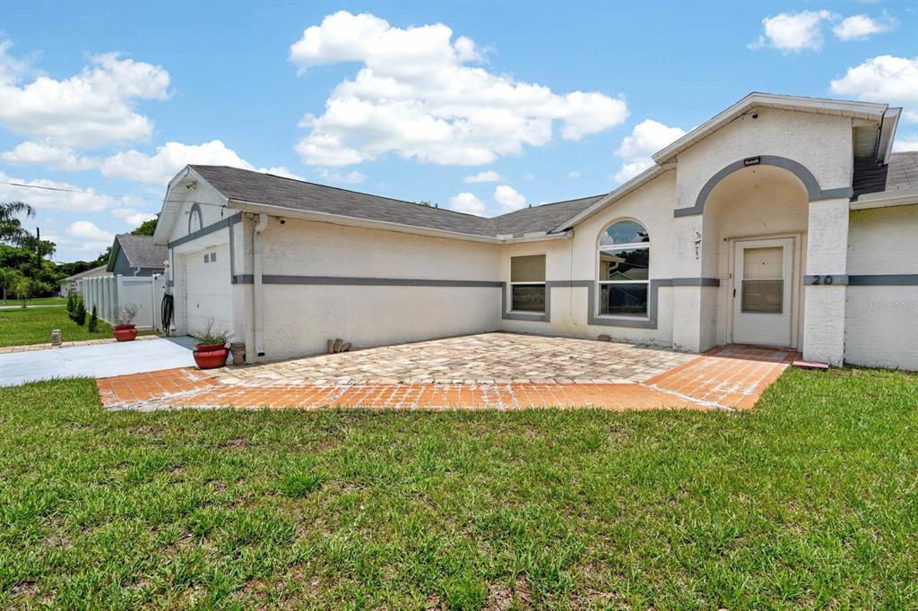 A single-story house with a white stucco exterior, a paved patio, and a front entrance — 20 LAKE MEADOW WAY, ORMOND BEACH, FL