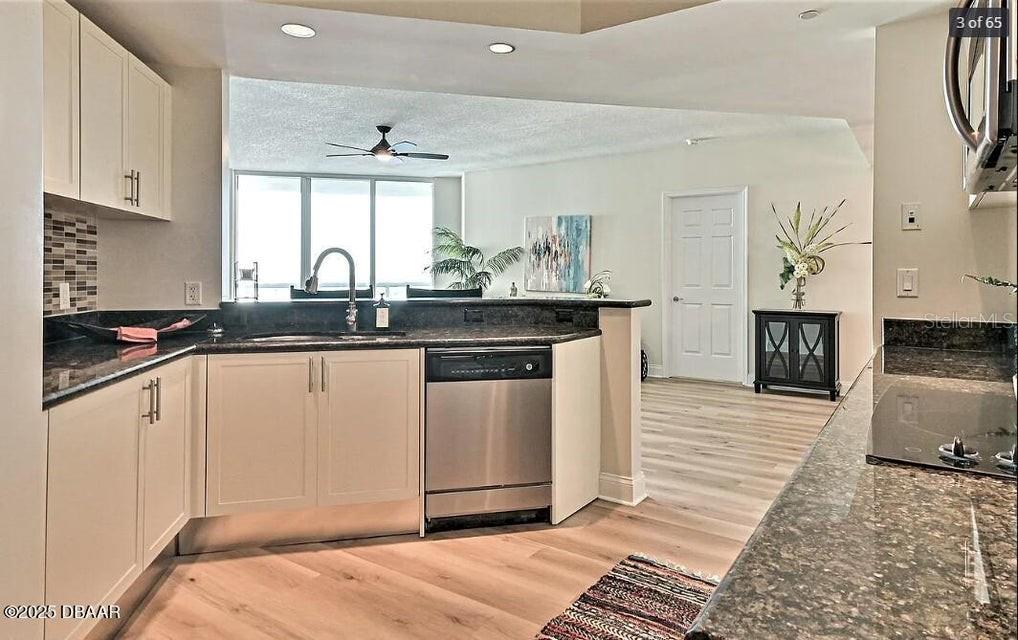 A kitchen with white cabinets, dark countertops, and stainless steel appliances overlooks a living area — 231 RIVERSIDE DRIVE UNIT 2206, HOLLY HILL, FL