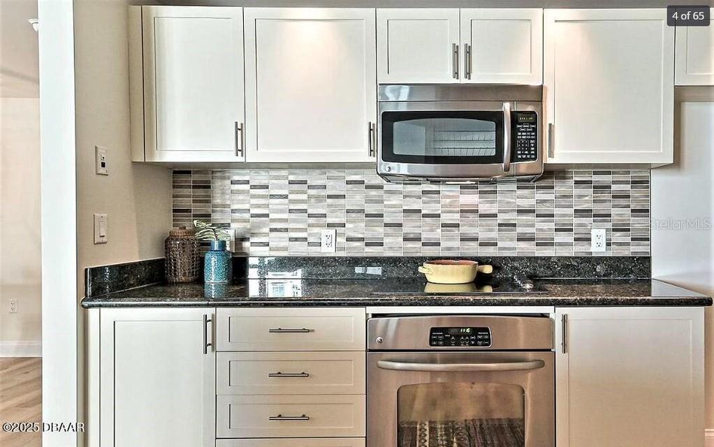 A kitchen features white cabinets, a stainless steel microwave, and a dark granite countertop — 231 RIVERSIDE DRIVE UNIT 2206, HOLLY HILL, FL