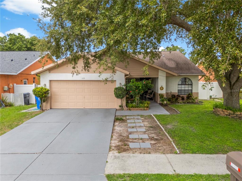A single-story house with a beige garage, a concrete driveway, and a large shade tree — 1215 RINKFIELD PLACE, BRANDON, FL