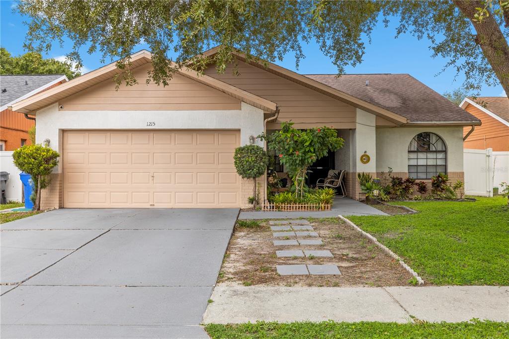 A single-story house with a beige stucco exterior, a two-car garage, and a front walkway — 1215 RINKFIELD PLACE, BRANDON, FL