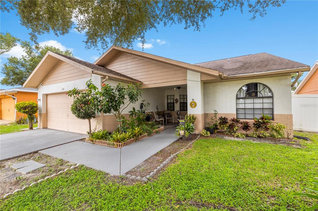 A single-story house with a tan exterior, a two-car garage, and a covered front porch — 1215 RINKFIELD PLACE, BRANDON, FL