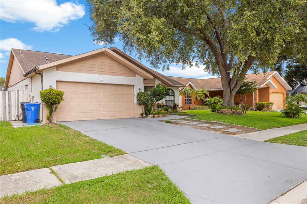 A single-story house with a beige garage, a concrete driveway, and a large oak tree — 1215 RINKFIELD PLACE, BRANDON, FL