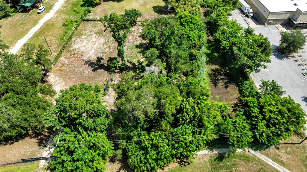 An aerial view shows a vacant, partially wooded lot adjacent to a commercial parking area — 9926 ROCKHILL ROAD, THONOTOSASSA, FL