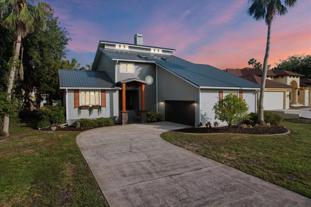 A two-story house with a metal roof, gray siding, and a concrete driveway at sunset — 5259 S STETSON POINT DRIVE, HOMOSASSA, FL