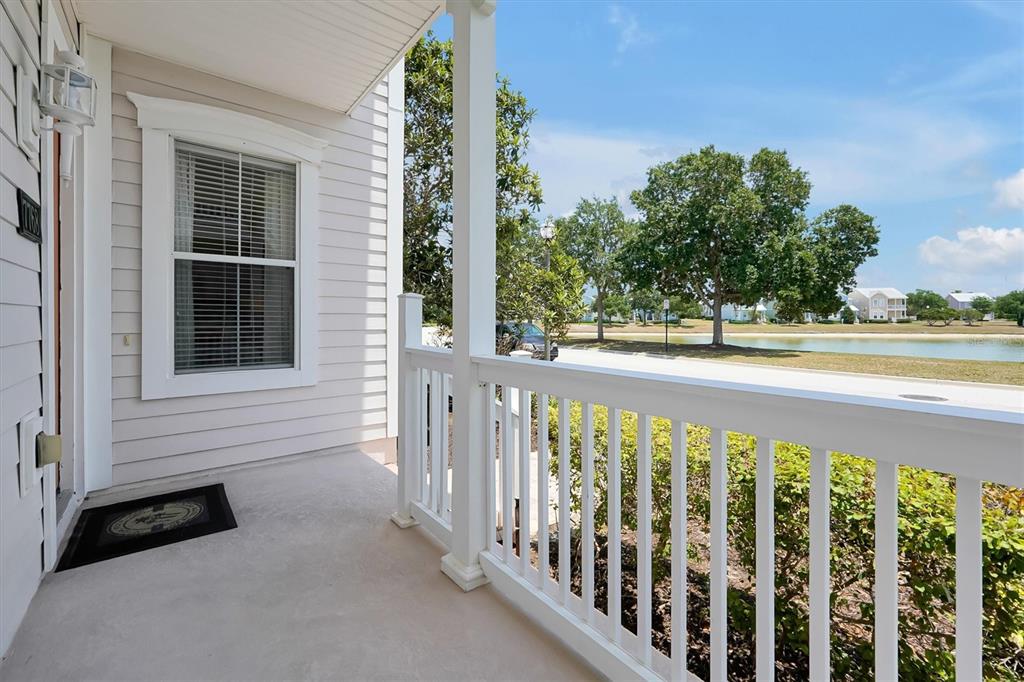 A covered front porch with a white railing overlooks a pond and neighborhood trees — 7768 LINKSIDE LOOP, REUNION, FL
