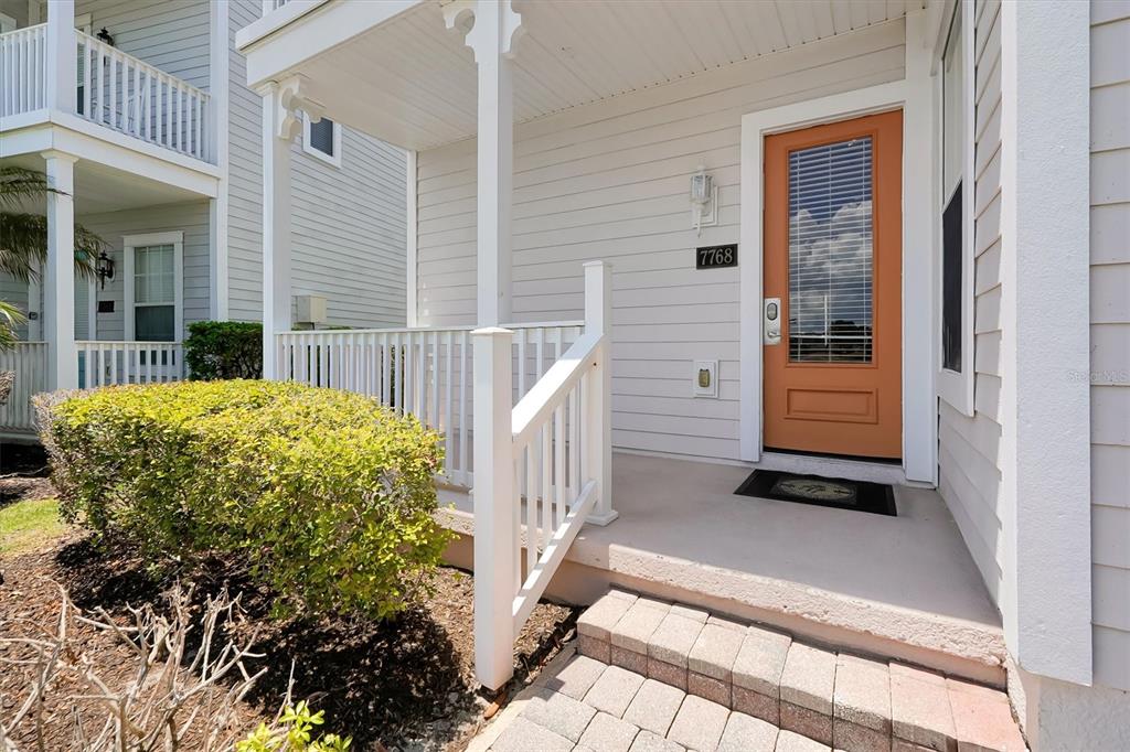 A front porch with a light-colored door, white railings, and a small bush — 7768 LINKSIDE LOOP, REUNION, FL