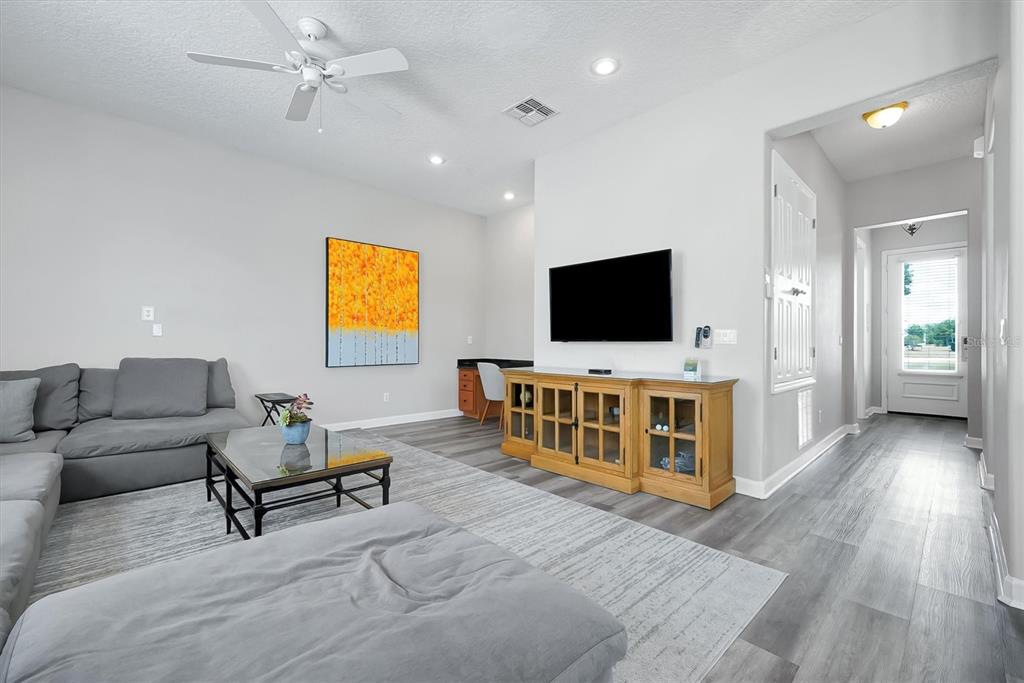 A living room features gray flooring, a sectional sofa, a television, and a wooden console — 7768 LINKSIDE LOOP, REUNION, FL