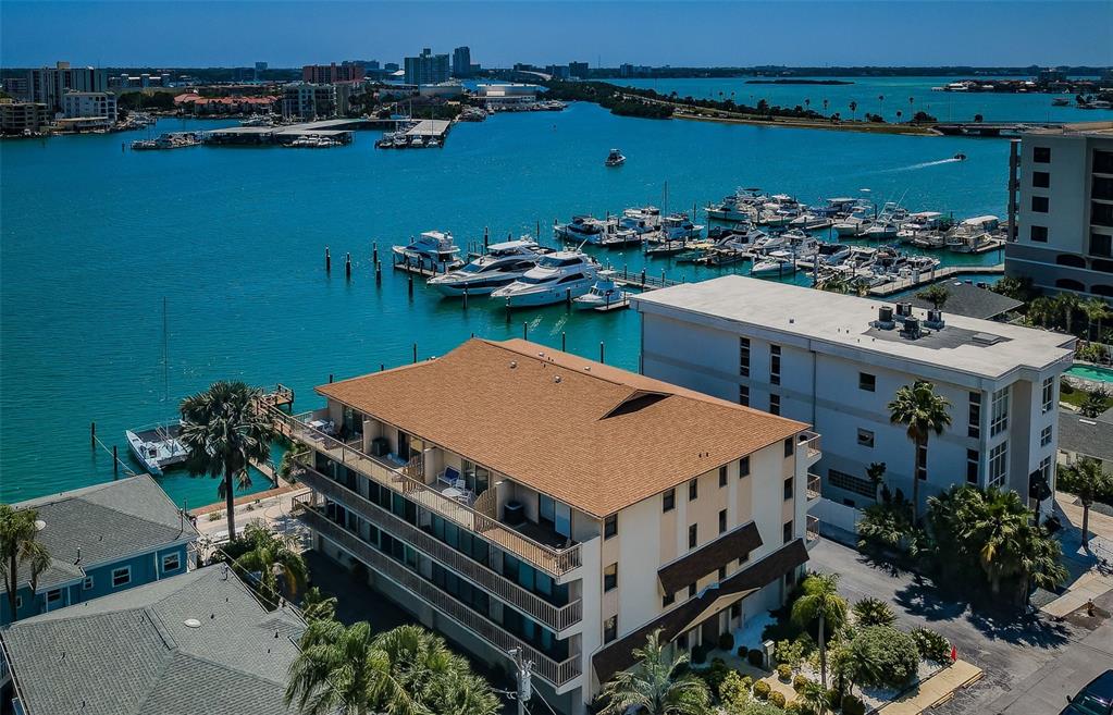 An aerial view shows a multi-story apartment building next to a marina with docked boats — 479 E SHORE DR UNIT 8, CLEARWATER, FL