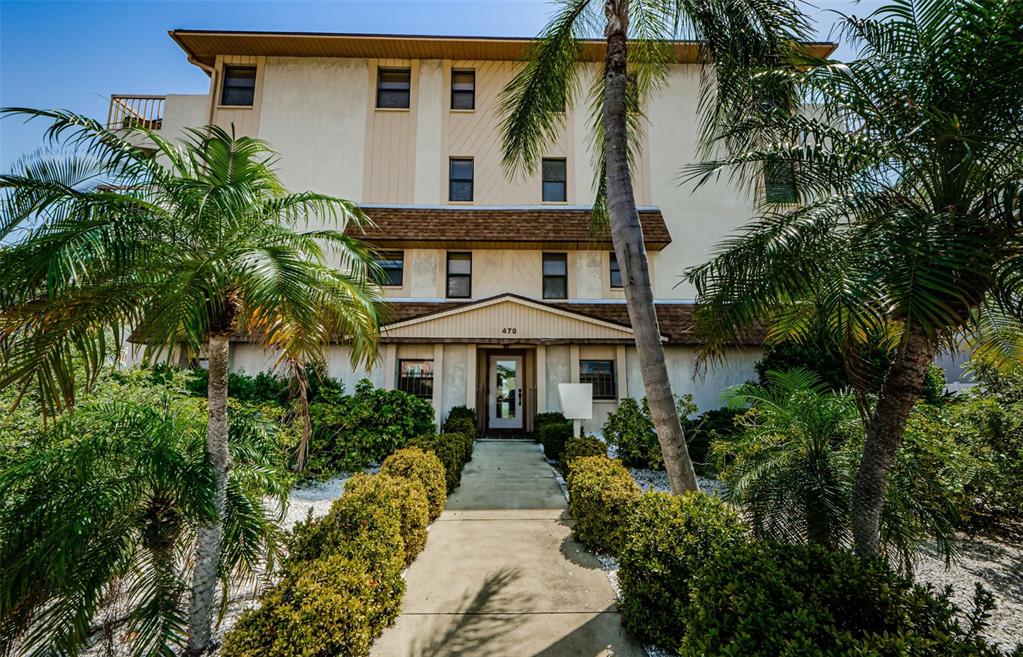 A three-story apartment building with a central entrance, palm trees, and landscaped bushes — 479 E SHORE DR UNIT 8, CLEARWATER, FL
