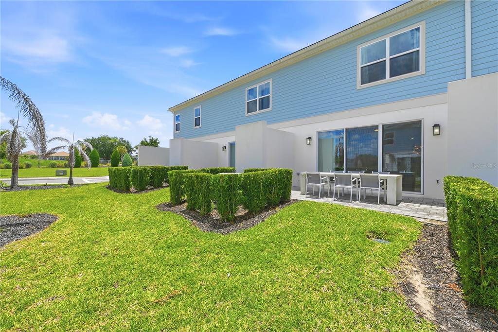 The exterior of a two-story townhouse features blue siding, a patio, and manicured hedges — 7857 SPECTRUM DRIVE, REUNION, FL