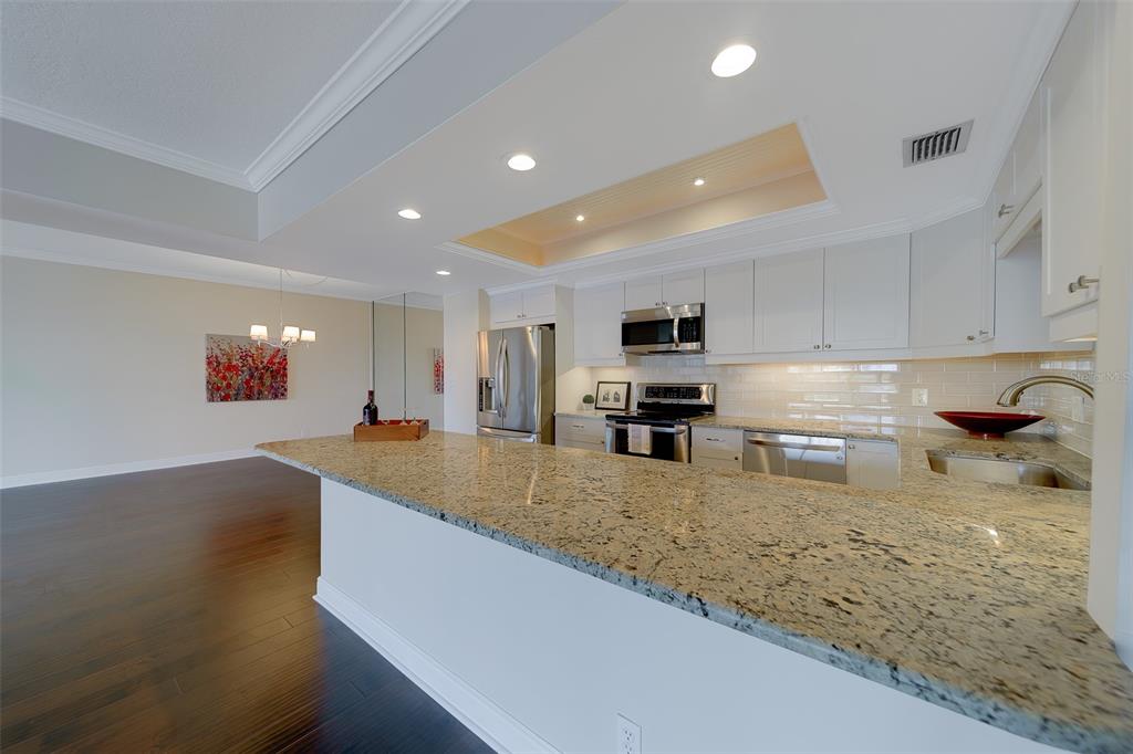 A kitchen with granite countertops, white cabinetry, and stainless steel appliances overlooks an open dining area — 8 BELLEVIEW BOULEVARD UNIT 308, BELLEAIR, FL