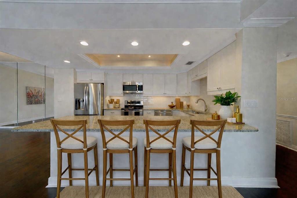 A kitchen with white cabinets, granite countertops, and four wooden bar stools at an island — 8 BELLEVIEW BOULEVARD UNIT 308, BELLEAIR, FL