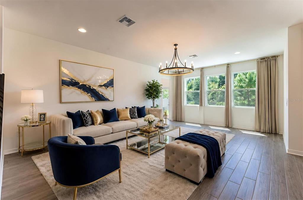 A living room features a beige sofa, blue accent chair, tufted ottoman, and large windows — 5675 GREEN ARROW PLACE, SANFORD, FL