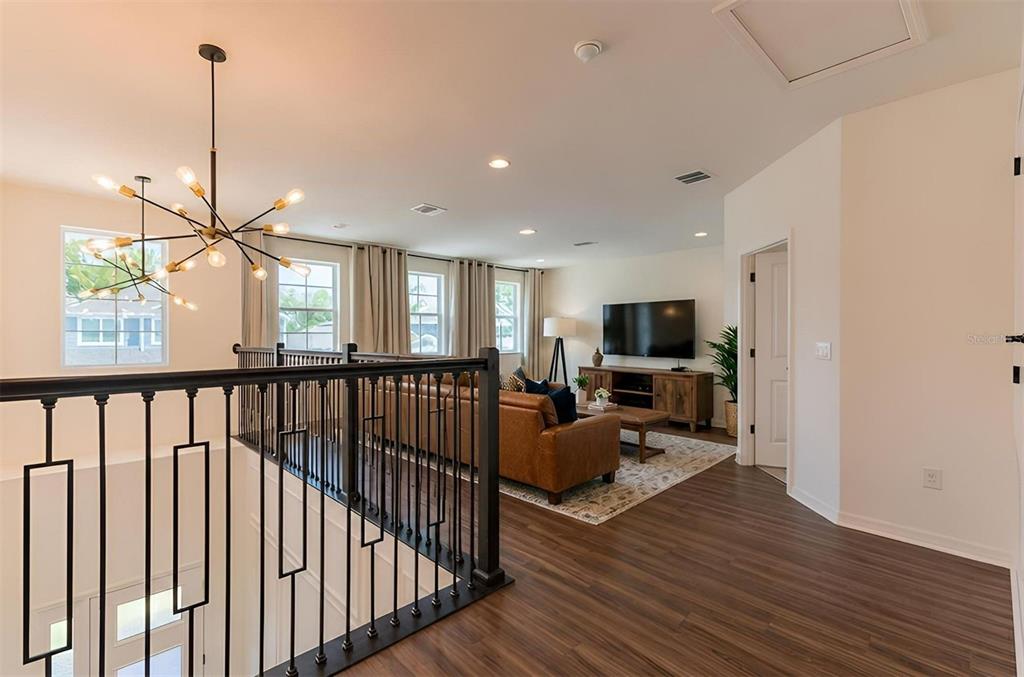A loft area features wood-look flooring, a modern chandelier, and a view into a living room — 5675 GREEN ARROW PLACE, SANFORD, FL