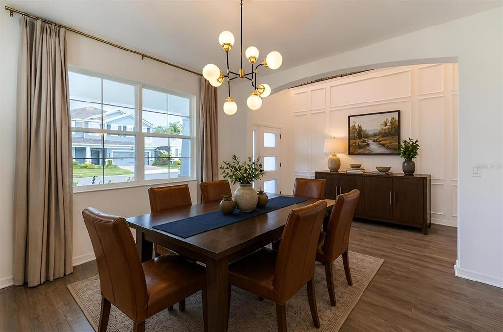 A dining room features a dark wood table, leather chairs, a modern chandelier, and wainscoting — 5675 GREEN ARROW PLACE, SANFORD, FL