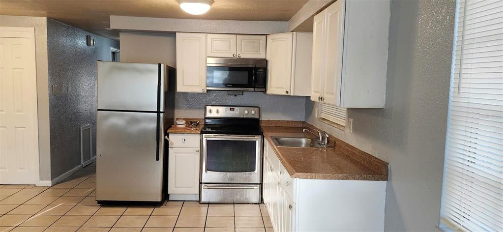 A kitchen features white cabinets, stainless steel appliances, and tan countertops over a tiled floor — 9809 N JASMINE AVENUE UNIT B, TAMPA, FL