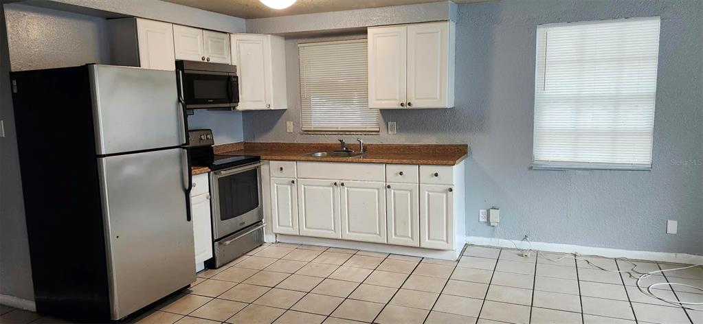 A kitchen with white cabinets, stainless steel appliances, a brown countertop, and tiled flooring — 9809 N JASMINE AVENUE UNIT B, TAMPA, FL