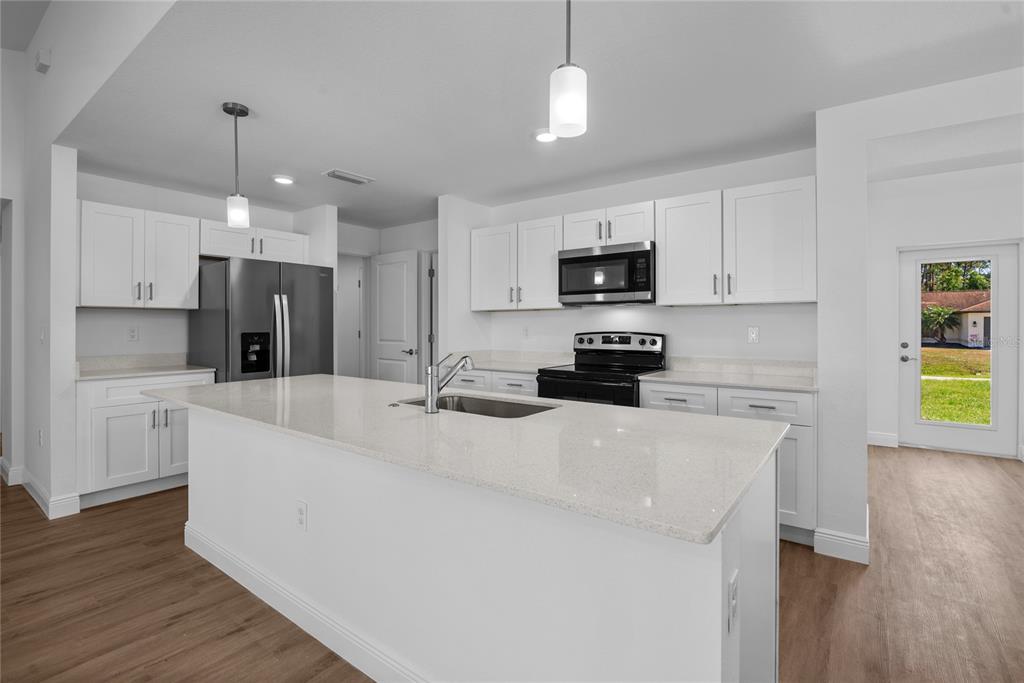 A modern kitchen features white cabinetry, a large quartz island with a sink, and stainless appliances — 23377 AVACADO AVENUE, PORT CHARLOTTE, FL