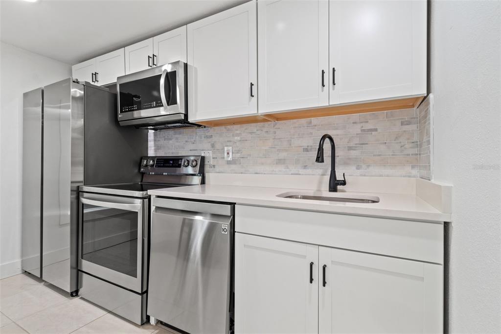 A kitchen features white cabinets, stainless steel appliances, a tiled backsplash, and a black faucet — 609 N OSCEOLA AVENUE UNIT A, CLEARWATER, FL