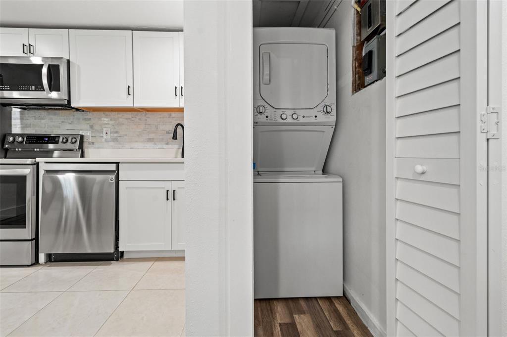 A kitchen with white cabinets and stainless steel appliances sits next to a stacked laundry unit — 609 N OSCEOLA AVENUE UNIT A, CLEARWATER, FL