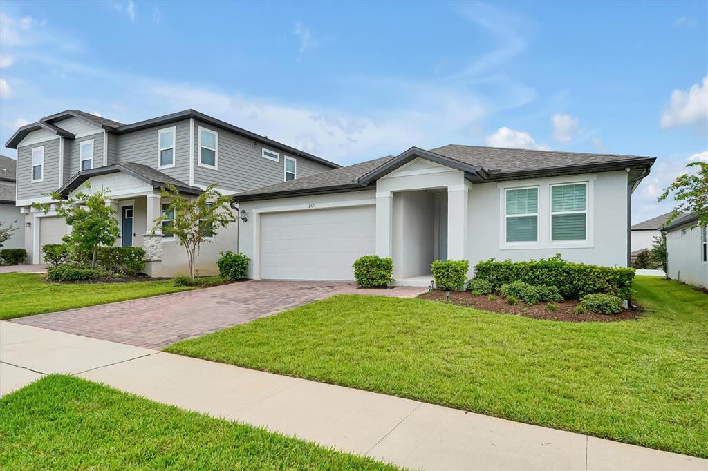 A single-story house with a white stucco exterior, a two-car garage, and a paved driveway — 2327 RAVEN RIDGE ROAD, MINNEOLA, FL