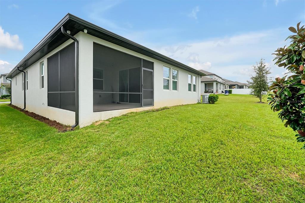 The exterior of a house features a screened-in patio and a large grassy backyard — 2327 RAVEN RIDGE ROAD, MINNEOLA, FL