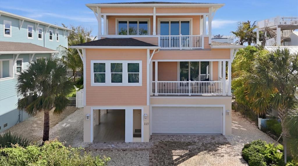 A three-story peach-colored house features a white garage, a covered balcony, and a paved driveway — 113 AQUA LANE, HOLMES BEACH, FL