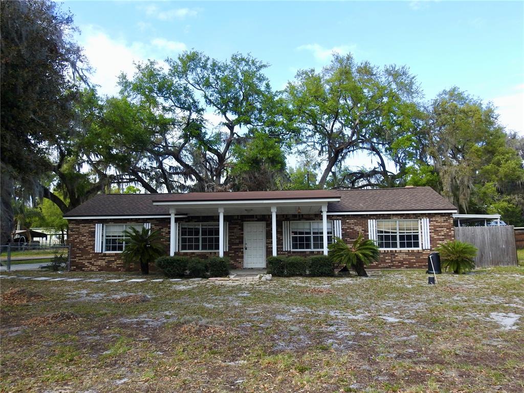 A single-story brick house with a covered front porch and large trees in the yard — 5107 COUNTY ROAD 163, WILDWOOD, FL