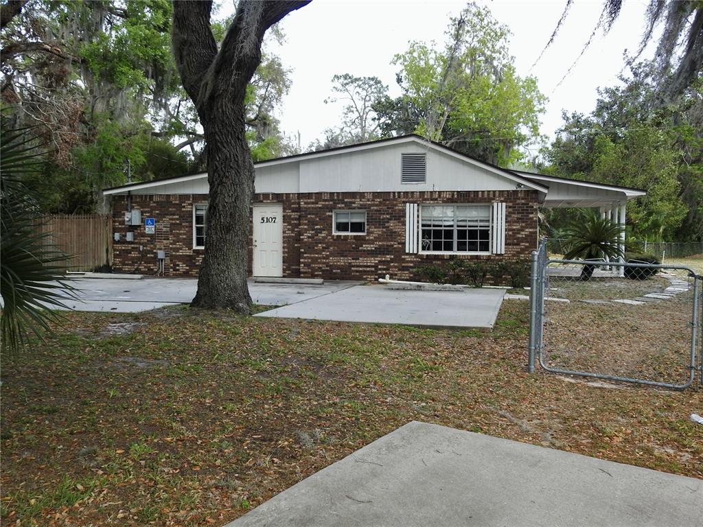 A single-story brick building features a white door, a carport, and a chain-link fence — 5107 COUNTY ROAD 163, WILDWOOD, FL