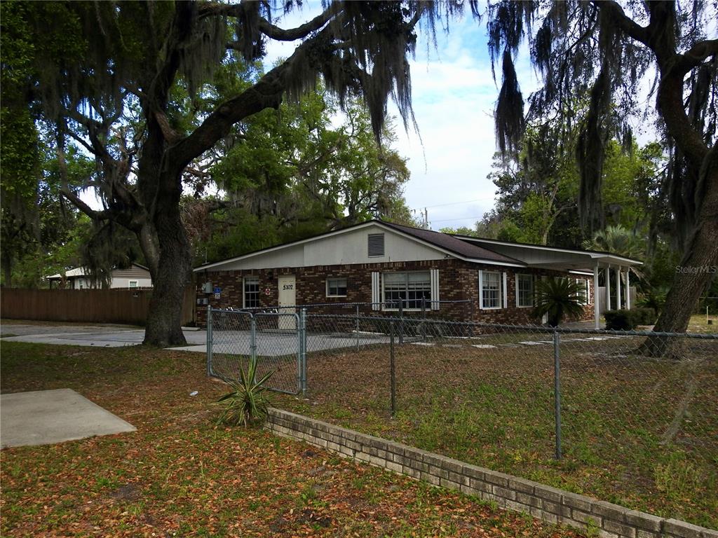 A single-story brick building with a chain-link fence and large moss-covered oak trees — 5107 COUNTY ROAD 163, WILDWOOD, FL