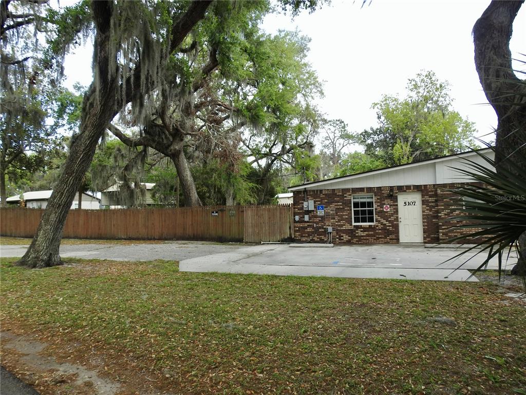 A brick building with a white door stands beside a wooden fence and large trees — 5107 COUNTY ROAD 163, WILDWOOD, FL