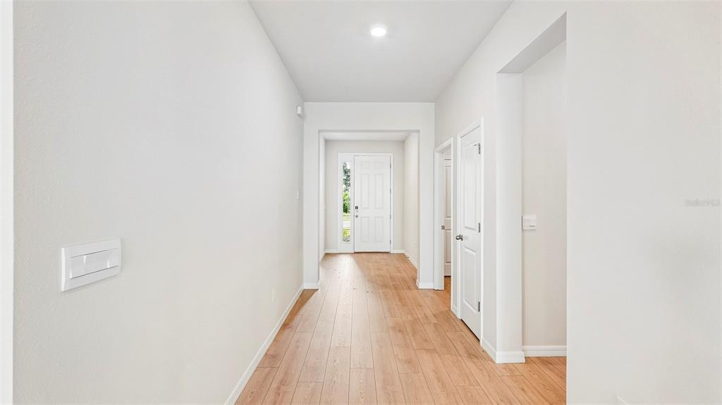 A bright hallway with light wood-look flooring leads to a white front door — 2032 VANDALIA PLACE, PARRISH, FL