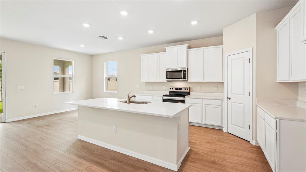 A modern kitchen features white cabinetry, a central island with a sink, and wood-look flooring — 2032 VANDALIA PLACE, PARRISH, FL