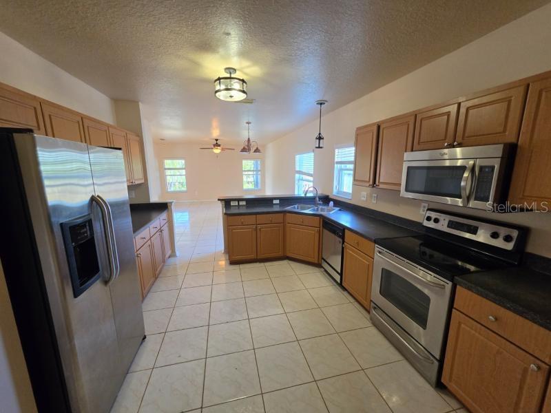 A kitchen with wood cabinets, stainless steel appliances, and tile flooring opens to a living area — 731 CRISTELLE JEAN DRIVE, RUSKIN, FL