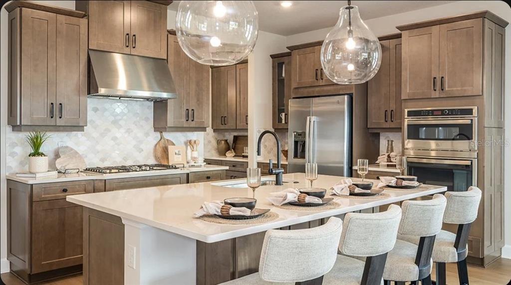 A kitchen features wood cabinets, stainless steel appliances, a large island, and globe pendant lights — 19357 LOCHSIDE LANE, MOUNT DORA, FL