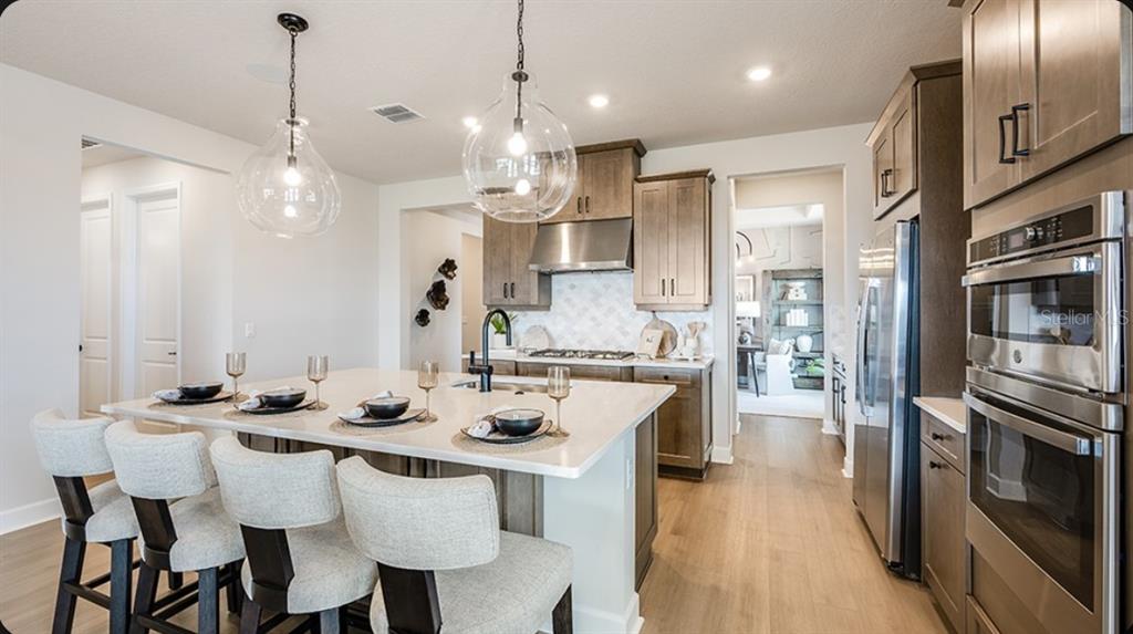 A kitchen features a large island with four chairs, stainless steel appliances, and wood cabinets — 19357 LOCHSIDE LANE, MOUNT DORA, FL